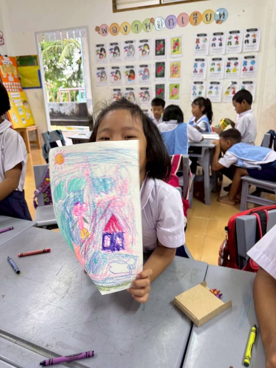 Student holding up a crayon drawing of a house